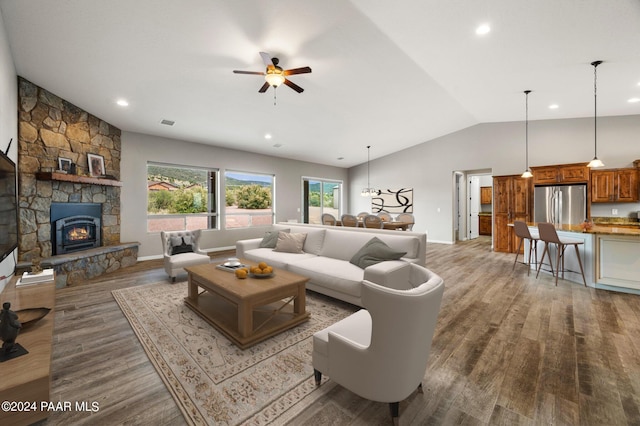 living room with wood-type flooring, a stone fireplace, ceiling fan, and lofted ceiling