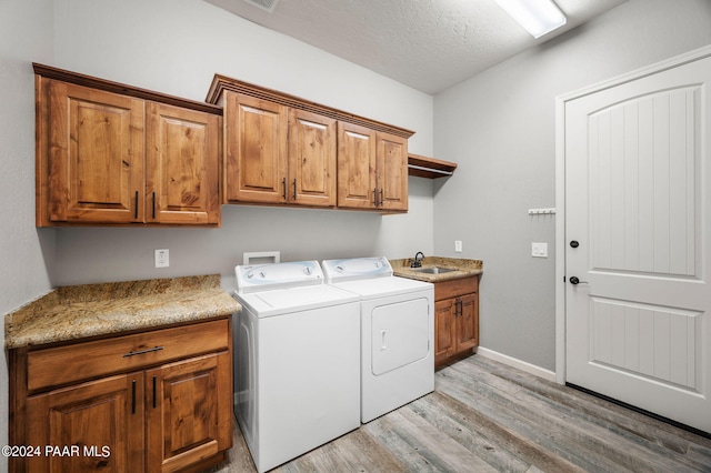 laundry room with cabinets, sink, separate washer and dryer, a textured ceiling, and light hardwood / wood-style floors