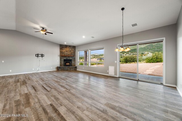 unfurnished living room featuring lofted ceiling, a stone fireplace, light wood-type flooring, and ceiling fan with notable chandelier