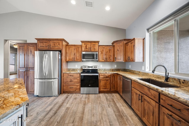 kitchen featuring lofted ceiling, sink, appliances with stainless steel finishes, light hardwood / wood-style floors, and light stone counters