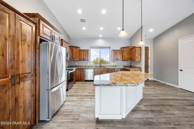 kitchen featuring pendant lighting, light wood-type flooring, appliances with stainless steel finishes, a kitchen island, and light stone counters