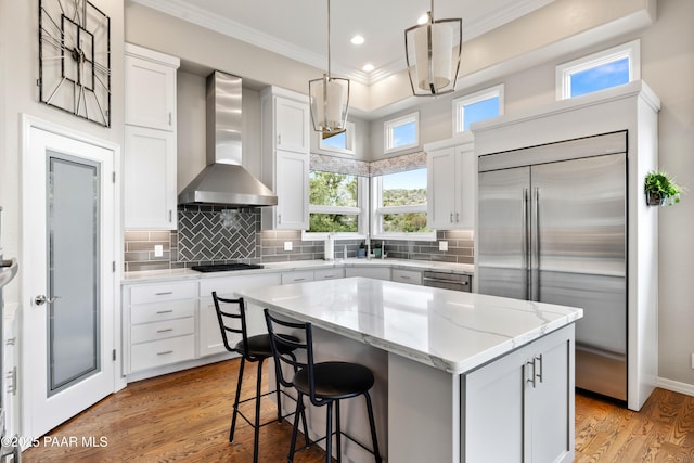 kitchen with crown molding, stainless steel appliances, a kitchen island, light wood finished floors, and wall chimney exhaust hood