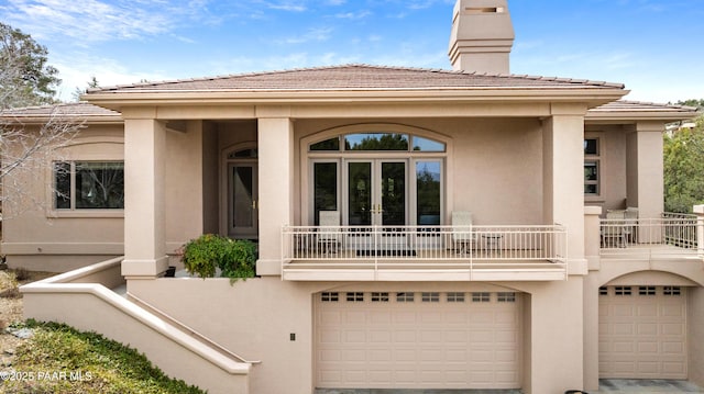 back of house with a tile roof, stucco siding, french doors, a balcony, and a garage