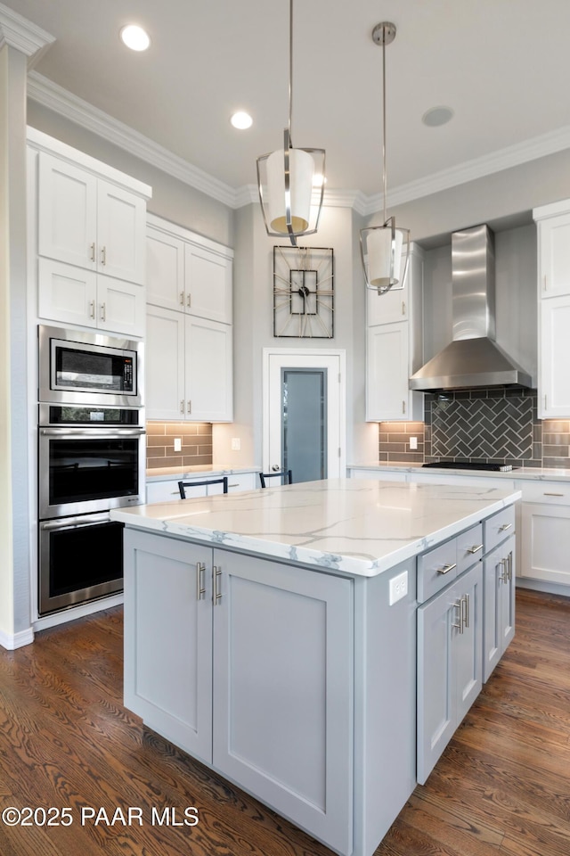 kitchen featuring white cabinetry, appliances with stainless steel finishes, a center island, wall chimney range hood, and dark wood-style flooring