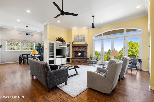 living area with wood finished floors, a stone fireplace, a healthy amount of sunlight, and ceiling fan
