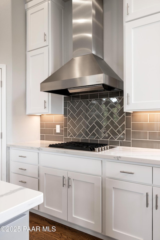 kitchen with wall chimney range hood, stainless steel gas stovetop, white cabinetry, and decorative backsplash