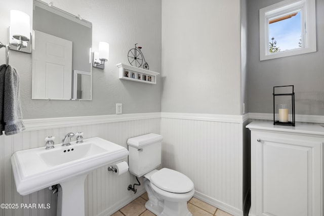 half bathroom featuring a wainscoted wall, toilet, and tile patterned flooring