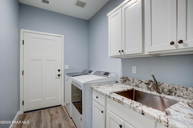 clothes washing area featuring cabinets, separate washer and dryer, light hardwood / wood-style flooring, and sink