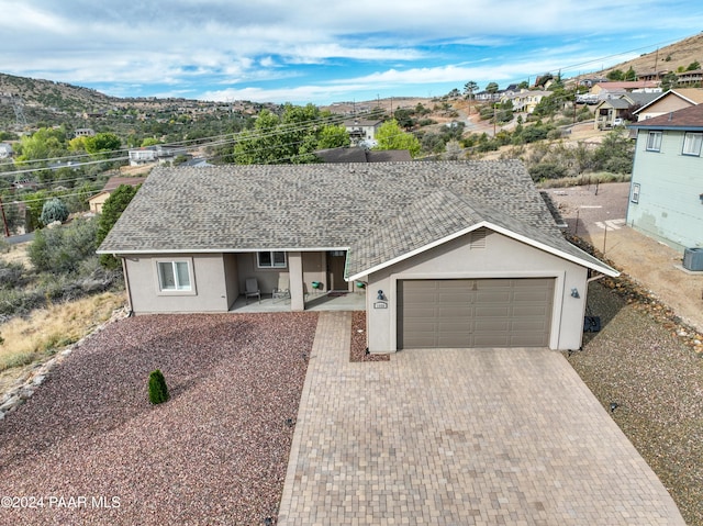 ranch-style home featuring a mountain view, a patio area, a garage, and central air condition unit