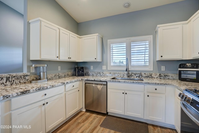 kitchen with sink, light stone counters, light hardwood / wood-style floors, white cabinets, and appliances with stainless steel finishes