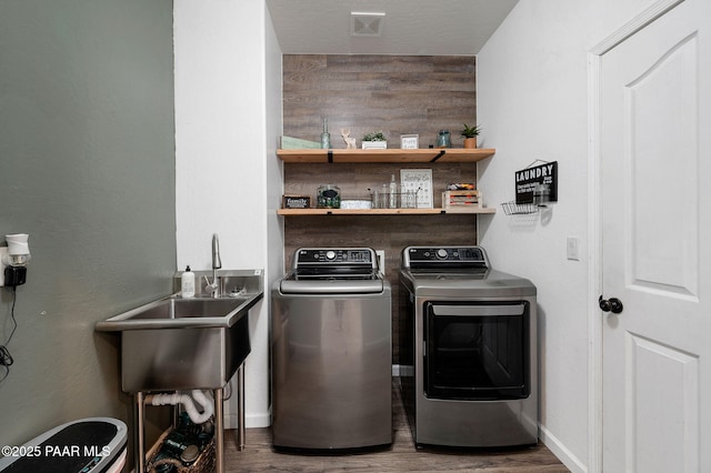 clothes washing area featuring wood-type flooring, wooden walls, washer and clothes dryer, and sink