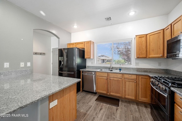 kitchen featuring light hardwood / wood-style floors, light stone countertops, sink, and black appliances