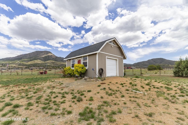 exterior space featuring fence, a rural view, a mountain view, and an outbuilding
