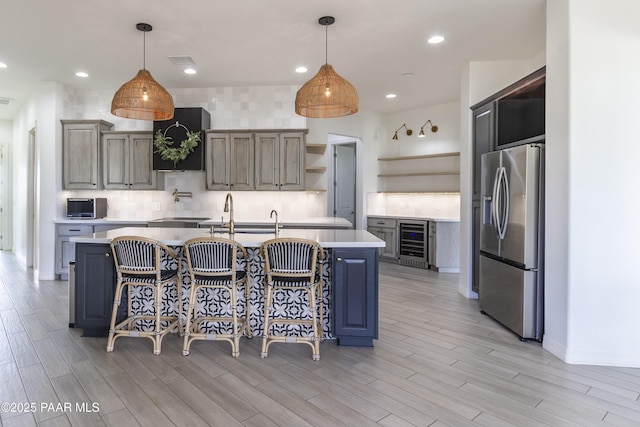 kitchen featuring beverage cooler, open shelves, stainless steel refrigerator with ice dispenser, light countertops, and an island with sink