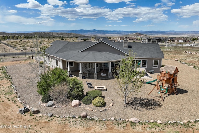 rear view of house featuring a playground, a patio, a mountain view, and fence