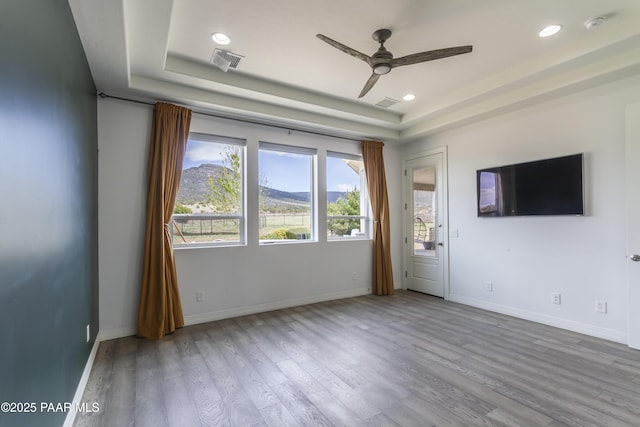 interior space with wood finished floors, visible vents, a ceiling fan, a tray ceiling, and baseboards