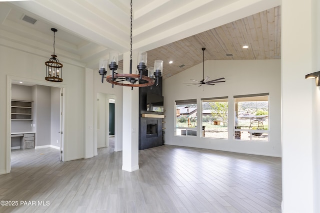 unfurnished living room with visible vents, ceiling fan with notable chandelier, a towering ceiling, wood finished floors, and a large fireplace