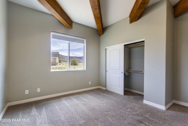 unfurnished bedroom featuring baseboards, beamed ceiling, carpet flooring, and a closet