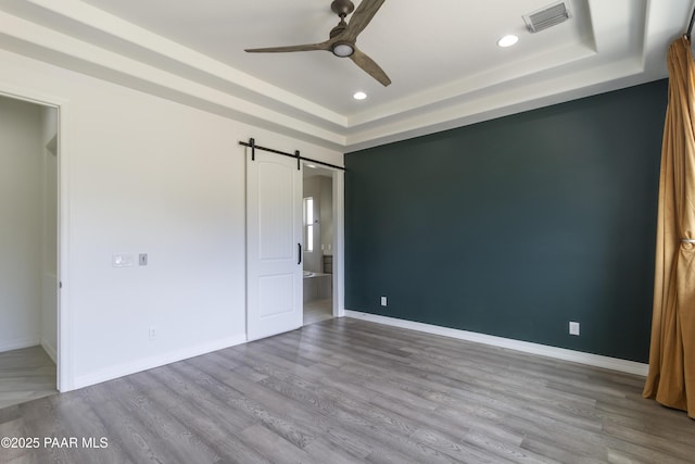 unfurnished bedroom featuring a raised ceiling, a barn door, visible vents, and wood finished floors