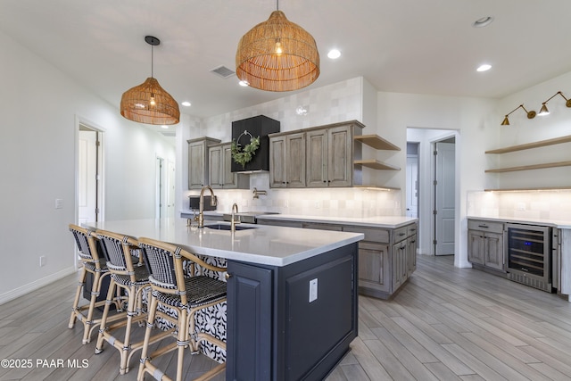 kitchen with wine cooler, a sink, open shelves, decorative backsplash, and a center island with sink