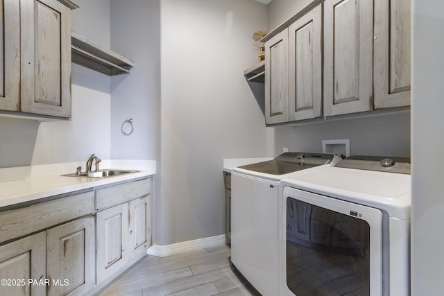 laundry room featuring light wood-style flooring, a sink, separate washer and dryer, cabinet space, and baseboards