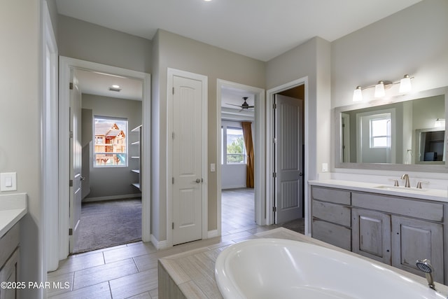 full bath with a garden tub, baseboards, vanity, and ceiling fan