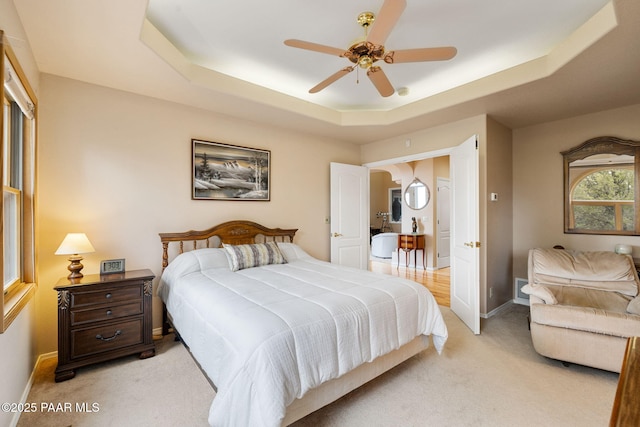 bedroom featuring light carpet, baseboards, a tray ceiling, and a ceiling fan