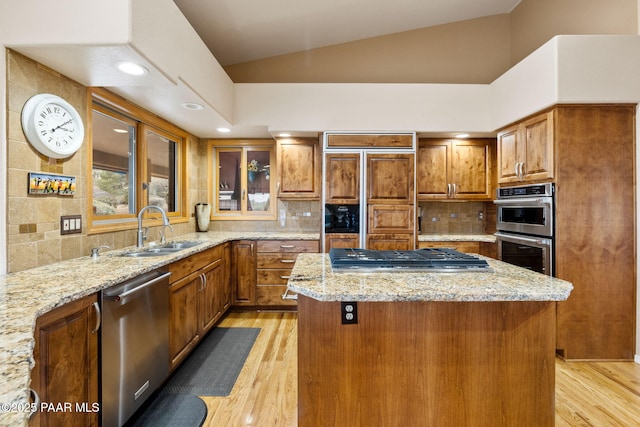kitchen with lofted ceiling, a sink, stainless steel appliances, brown cabinets, and a center island