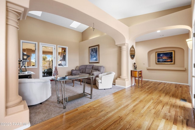 living room featuring baseboards, a skylight, wood finished floors, arched walkways, and ornate columns