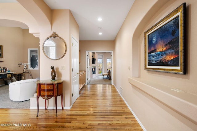 corridor featuring light wood finished floors, visible vents, baseboards, recessed lighting, and arched walkways