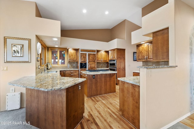 kitchen featuring a peninsula, light stone counters, brown cabinets, and a sink
