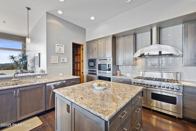 kitchen featuring wall chimney range hood, sink, stainless steel appliances, light stone countertops, and decorative light fixtures