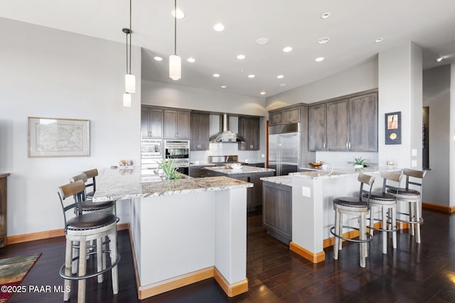 kitchen with pendant lighting, built in appliances, light stone counters, and dark brown cabinets