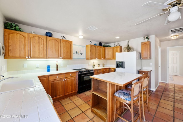 kitchen featuring black gas range, visible vents, tile counters, a sink, and white fridge with ice dispenser