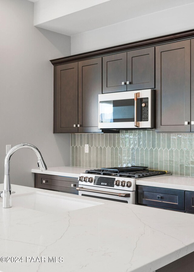 kitchen with gas range oven, dark brown cabinetry, tasteful backsplash, and sink