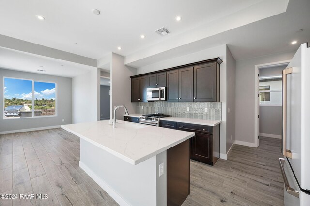 kitchen with sink, light stone counters, a center island with sink, appliances with stainless steel finishes, and light wood-type flooring