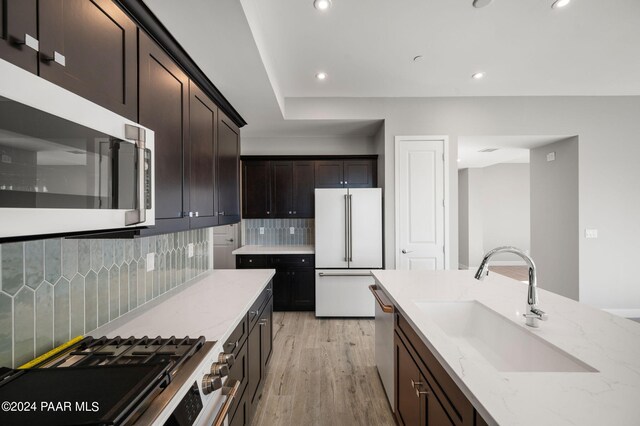 kitchen featuring high end appliances, backsplash, sink, light hardwood / wood-style floors, and light stone counters