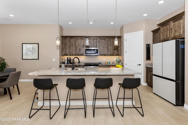 kitchen featuring dark brown cabinetry, appliances with stainless steel finishes, light wood-style floors, a kitchen bar, and a sink