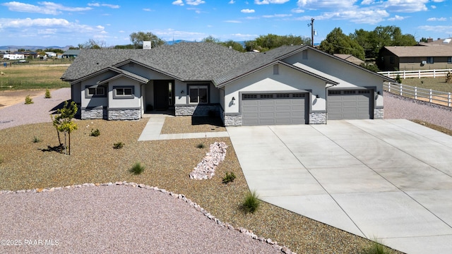 view of front facade with stucco siding, concrete driveway, an attached garage, fence, and stone siding