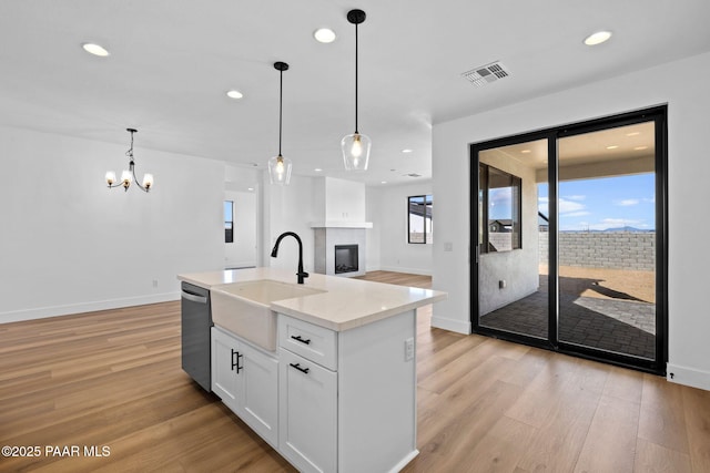 kitchen with white cabinetry, sink, hanging light fixtures, and an island with sink