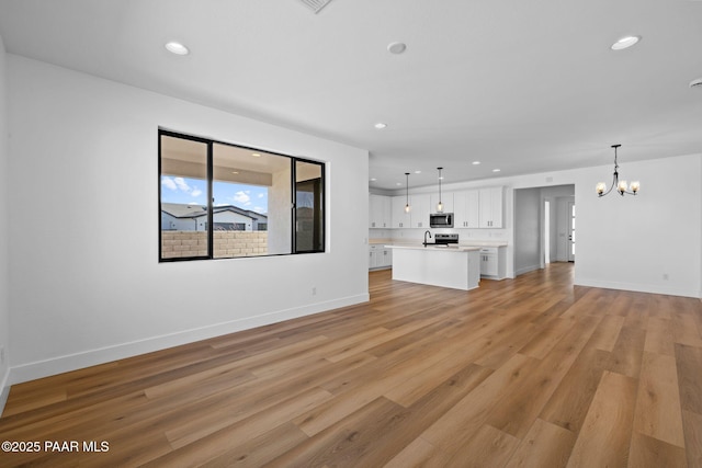 unfurnished living room featuring sink, a chandelier, and light hardwood / wood-style floors