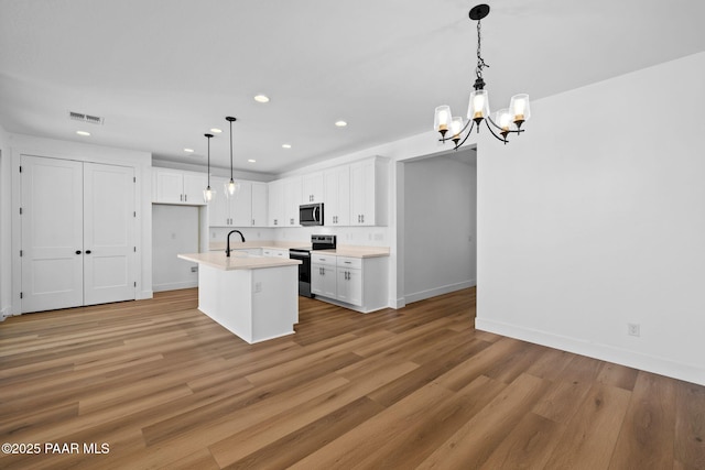 kitchen featuring hanging light fixtures, stainless steel appliances, an inviting chandelier, an island with sink, and white cabinets