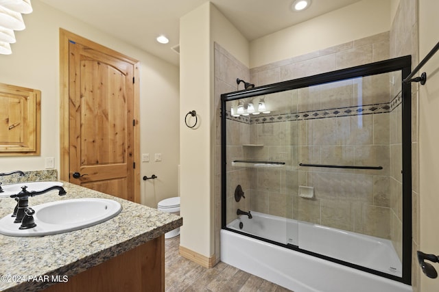 full bathroom with vanity, hardwood / wood-style flooring, shower / bath combination with glass door, and toilet