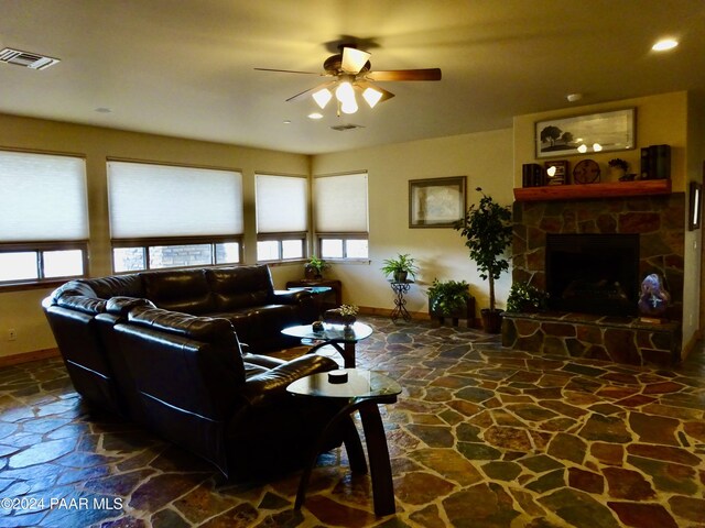 living room featuring ceiling fan, plenty of natural light, and a stone fireplace