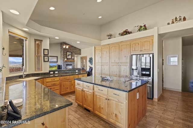 kitchen with dark stone countertops, sink, a center island with sink, and stainless steel fridge