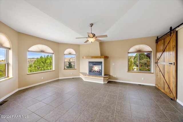 unfurnished living room with ceiling fan, a large fireplace, a barn door, and dark tile patterned floors