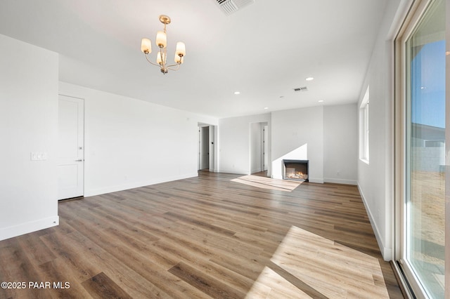 unfurnished living room with hardwood / wood-style flooring, an inviting chandelier, and a healthy amount of sunlight