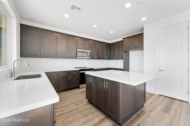 kitchen with sink, light hardwood / wood-style flooring, appliances with stainless steel finishes, dark brown cabinets, and a kitchen island