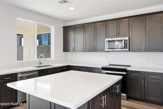 kitchen featuring dark brown cabinetry, sink, stainless steel appliances, a kitchen island, and light wood-type flooring