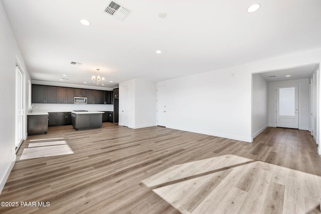 unfurnished living room with sink, a chandelier, and light hardwood / wood-style floors